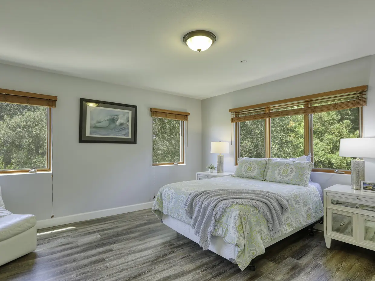 Bedroom at Avila Beach Gem with white bedding and corner windows onto the hillside
