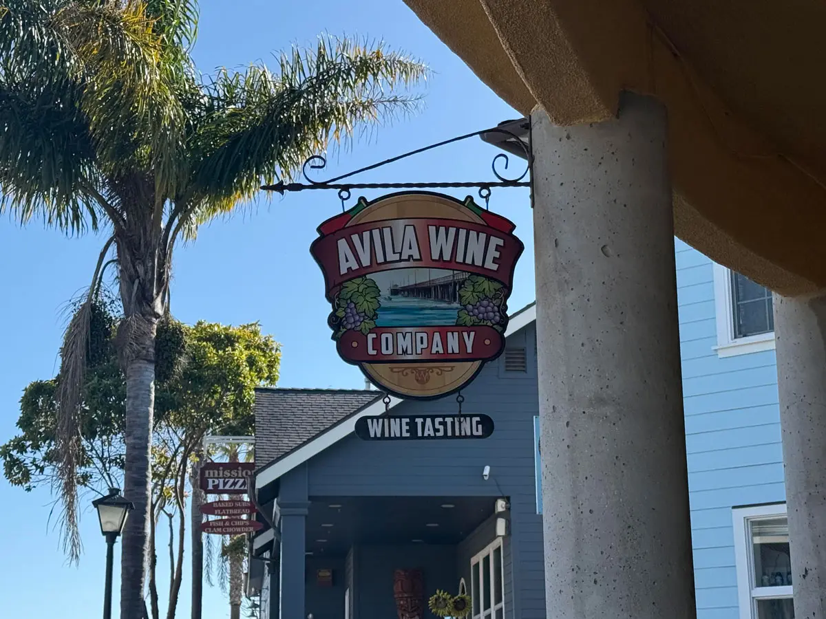 avila-wine-co The hanging sign for Avila Wine Company, painted with the pier and bunches of grapes, above a smaller sign reading Wine Tasting