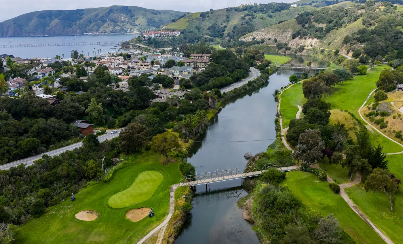 An aerial view along San Luis Creek with golf course fairways on both banks and the pier beyond