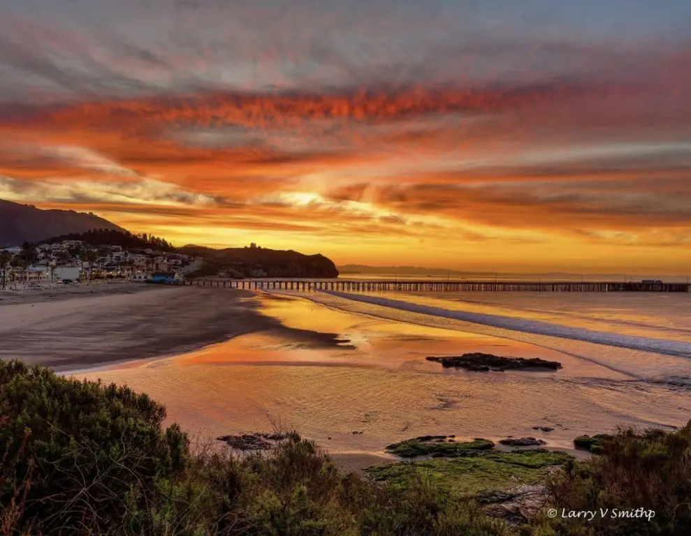 Sunset over Avila Beach with the pier silhouetted against an orange sky and wet sand reflecting the light