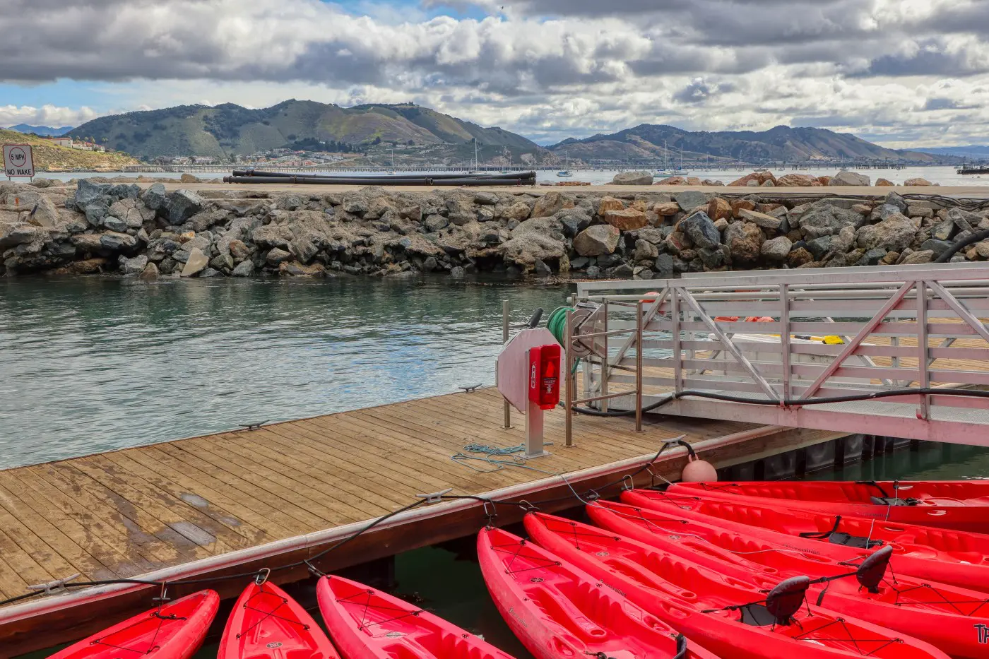 Red rental kayaks tied along the floating dock at Port San Luis, with the breakwater behind